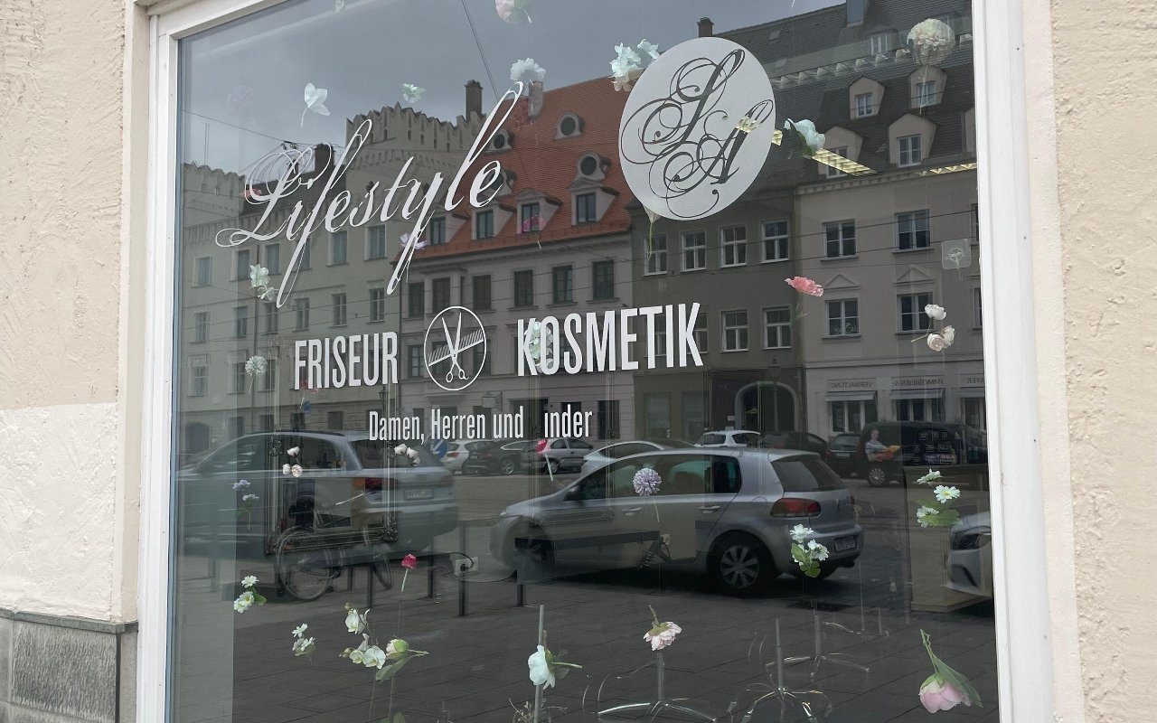 Schaufenster des Lifestyle-Ink Studios in Augsburg mit der Wortmarke „Lifestyle · Friseur · Kosmetik“ auf der Scheibe.